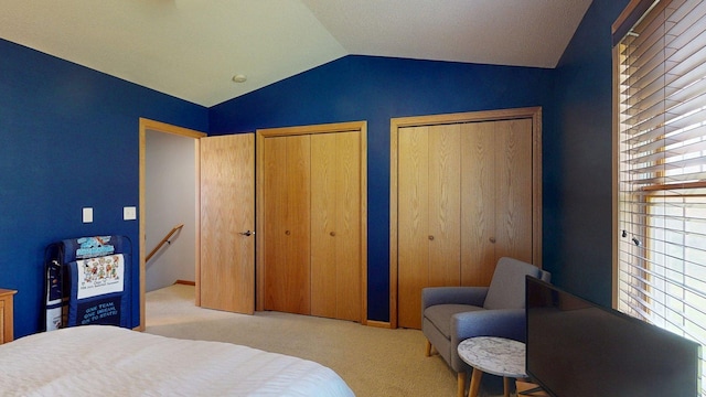 bedroom with vaulted ceiling, carpet flooring, and two closets
