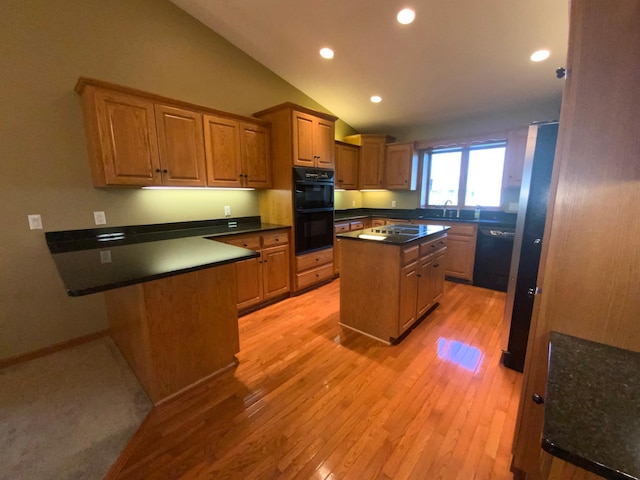 kitchen with black appliances, a sink, vaulted ceiling, light wood-type flooring, and dark countertops