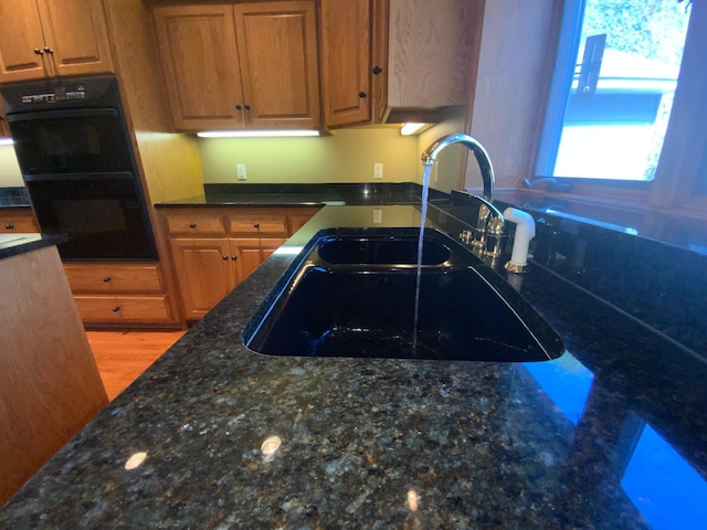 kitchen with a sink, dark stone counters, brown cabinetry, and light wood-style flooring