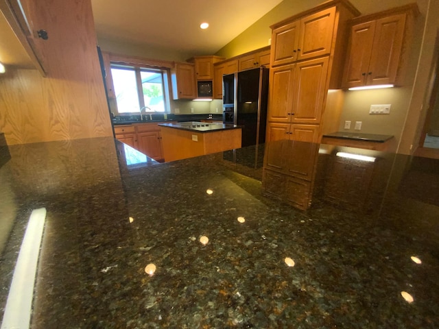 kitchen featuring black appliances, lofted ceiling, dark stone counters, brown cabinetry, and a kitchen island