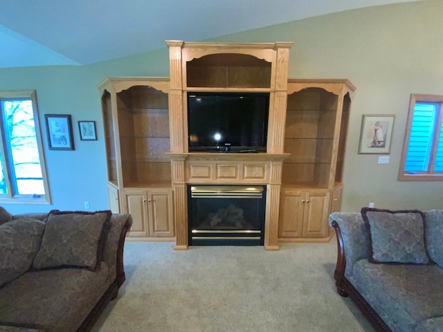 living area with vaulted ceiling, healthy amount of natural light, light colored carpet, and a glass covered fireplace