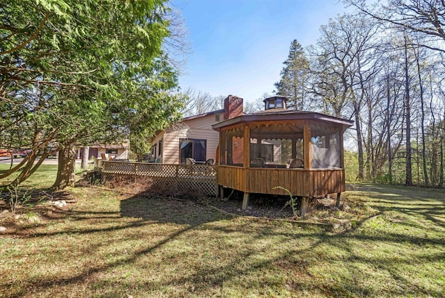 rear view of property featuring a gazebo, a yard, a deck, and a chimney
