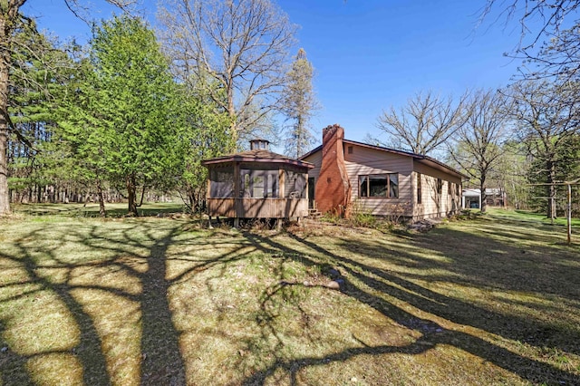 rear view of house with a chimney, a sunroom, and a yard