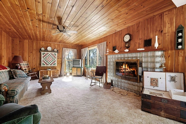 carpeted living room with wooden walls, wood ceiling, a tiled fireplace, and ceiling fan