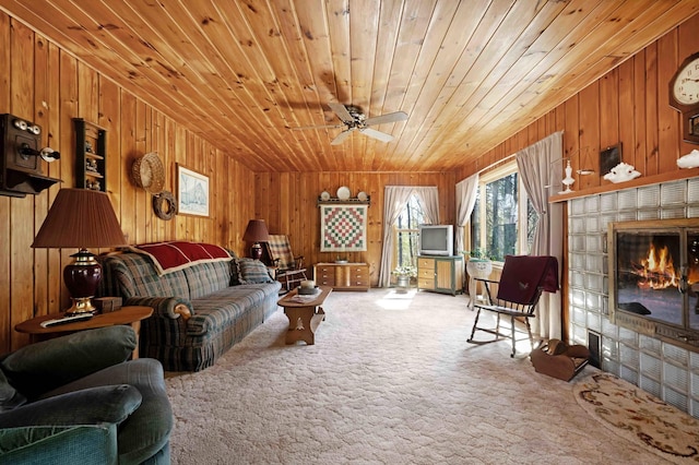 carpeted living area featuring wooden walls, ceiling fan, wood ceiling, and a glass covered fireplace