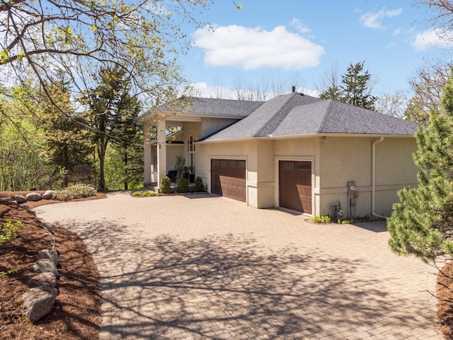 view of front of house with an attached garage, stucco siding, decorative driveway, and a shingled roof