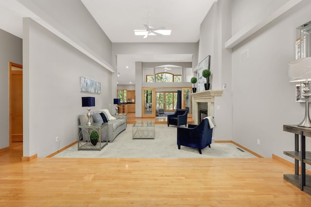 living room featuring a glass covered fireplace, a high ceiling, baseboards, ceiling fan, and wood finished floors