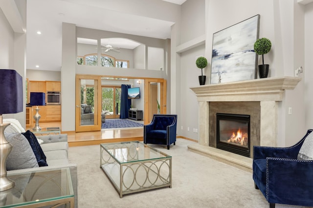 carpeted living area featuring a ceiling fan, a fireplace, recessed lighting, a high ceiling, and french doors