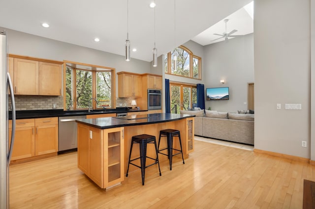 kitchen featuring appliances with stainless steel finishes, a center island, light wood finished floors, a breakfast bar area, and dark countertops