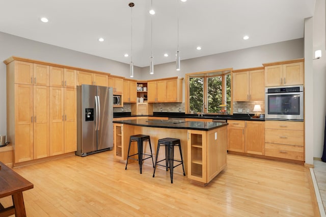 kitchen featuring stainless steel appliances, light brown cabinetry, open shelves, dark countertops, and a center island