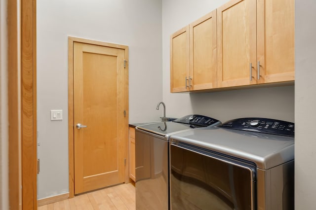 clothes washing area with washing machine and dryer, cabinet space, and light wood-style floors
