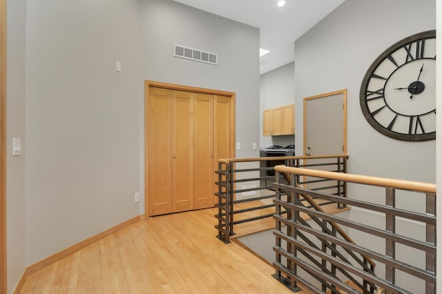 hallway with a towering ceiling, light wood-type flooring, an upstairs landing, baseboards, and recessed lighting