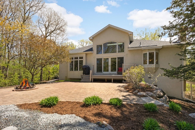 rear view of property featuring a patio, stucco siding, an outdoor fire pit, and roof with shingles