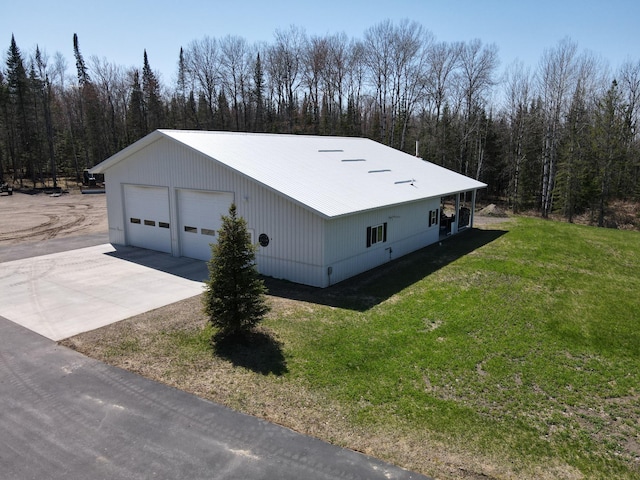 view of side of property featuring a garage, a view of trees, a lawn, metal roof, and an outdoor structure