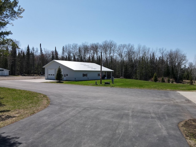 view of home's exterior with a yard, asphalt driveway, a forest view, and an outdoor structure