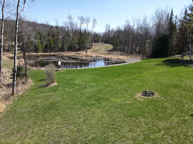 view of green lawn featuring a water view and a wooded view