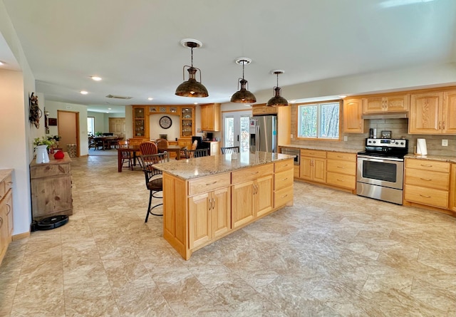 kitchen featuring stainless steel appliances, light brown cabinets, a kitchen breakfast bar, a kitchen island, and under cabinet range hood