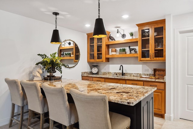 kitchen featuring open shelves, a sink, brown cabinetry, a kitchen breakfast bar, and decorative light fixtures