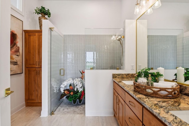 full bath with tiled shower, double vanity, and baseboards
