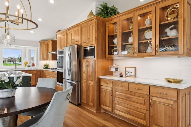 kitchen with stainless steel appliances, a chandelier, backsplash, light wood-style flooring, and brown cabinetry