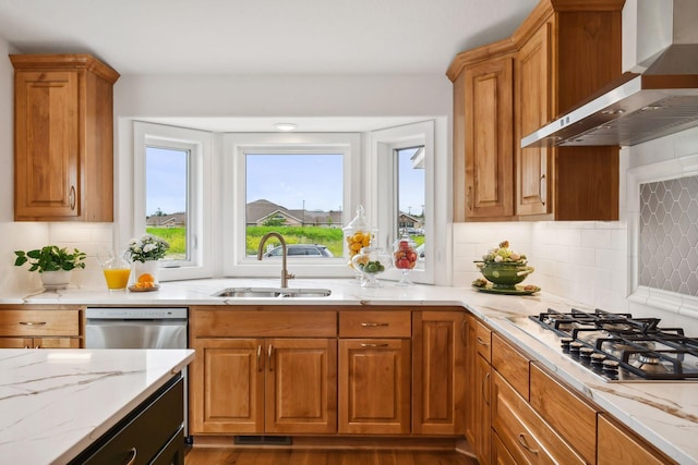 kitchen with wall chimney range hood, a sink, appliances with stainless steel finishes, light stone countertops, and tasteful backsplash
