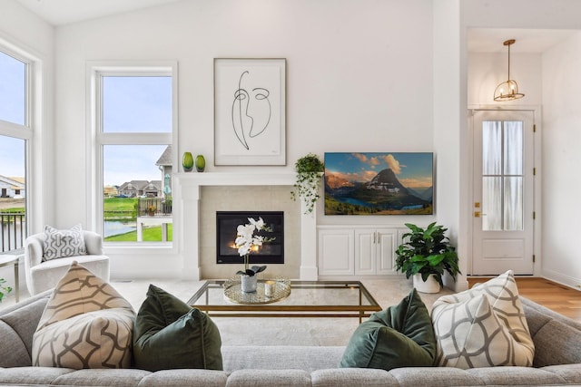 living room featuring healthy amount of natural light, wood finished floors, vaulted ceiling, a tiled fireplace, and baseboards