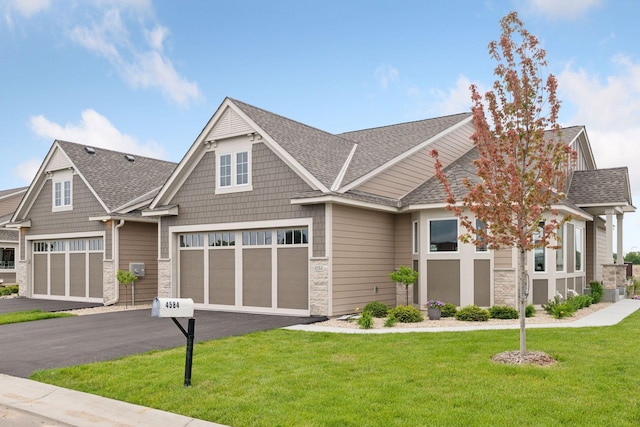 craftsman-style home featuring stone siding, a shingled roof, a front yard, and driveway