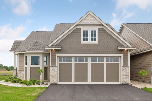 view of front of property featuring stone siding, driveway, an attached garage, and roof with shingles