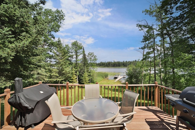 deck with grilling area, a water view, outdoor dining space, and view of scattered trees
