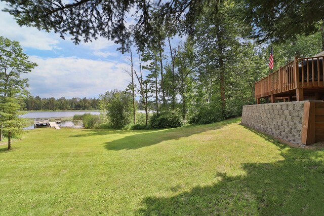 view of grassy yard featuring a deck with water view
