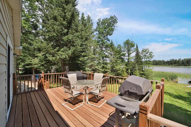 wooden deck with outdoor dining area, a water view, a lawn, grilling area, and view of wooded area