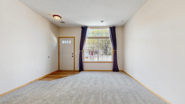 empty room featuring light carpet, a textured ceiling, and baseboards