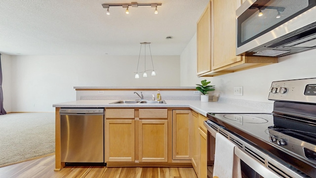 kitchen with stainless steel appliances, a sink, a peninsula, light countertops, and hanging light fixtures