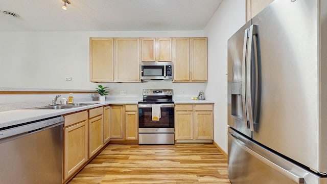 kitchen with appliances with stainless steel finishes, a sink, and light brown cabinetry