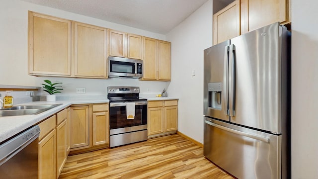 kitchen featuring appliances with stainless steel finishes, light brown cabinets, light wood-style flooring, light countertops, and a sink