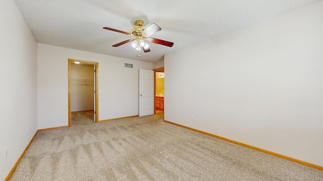 unfurnished bedroom with baseboards, light carpet, a walk in closet, a closet, and a ceiling fan