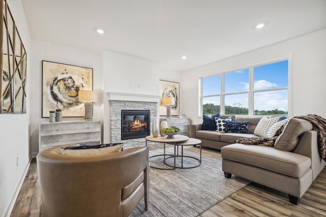 living room with wood finished floors, a stone fireplace, recessed lighting, and baseboards