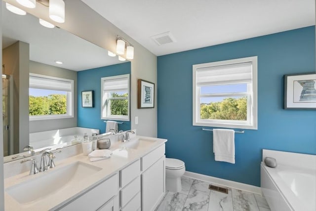 full bathroom featuring a garden tub, marble look tiles, baseboards, double vanity, and toilet