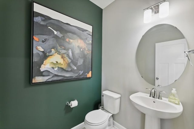 half bathroom with baseboards, toilet, and a sink