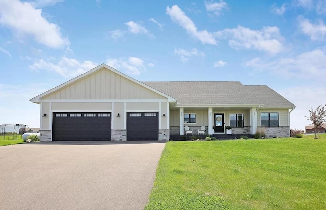 view of front of home featuring covered porch, asphalt driveway, a front lawn, an attached garage, and stone siding