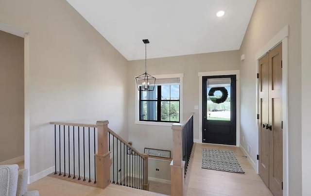 entryway featuring vaulted ceiling, baseboards, a chandelier, and light wood finished floors