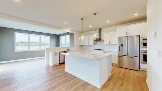kitchen with appliances with stainless steel finishes, wall chimney range hood, light countertops, light wood-style flooring, and recessed lighting