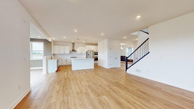 unfurnished living room featuring a sink, stairs, light wood-type flooring, baseboards, and recessed lighting