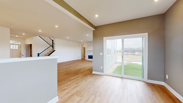 unfurnished room featuring light wood-style flooring, stairway, recessed lighting, baseboards, and a stone fireplace