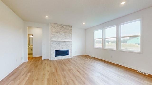 unfurnished living room featuring light wood-style flooring, baseboards, recessed lighting, and a stone fireplace