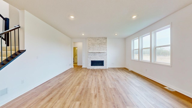 unfurnished living room with light wood finished floors, stairs, a stone fireplace, baseboards, and recessed lighting