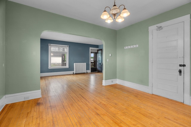822 35th St, Minneapolis, MN 55408 - empty room with arched walkways, radiator, baseboards, a chandelier, and hardwood / wood-style floors