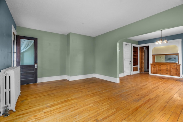 822 35th St, Minneapolis, MN 55408 - unfurnished room with radiator, light wood-type flooring, a chandelier, baseboards, and arched walkways