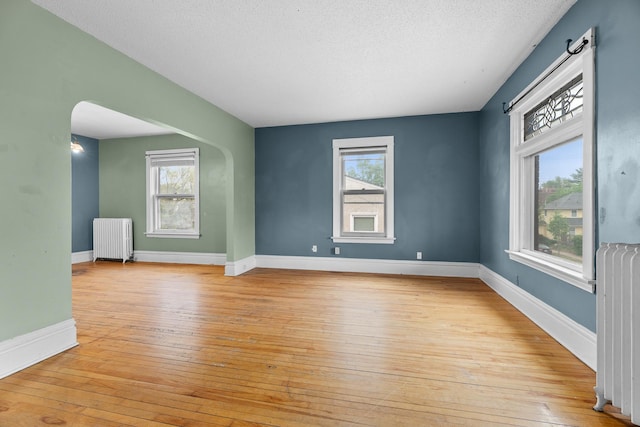 822 35th St, Minneapolis, MN 55408 - unfurnished room with radiator heating unit, arched walkways, light wood-style flooring, and a textured ceiling
