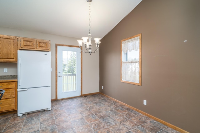 kitchen with freestanding refrigerator, baseboards, lofted ceiling, a chandelier, and stone finish floors